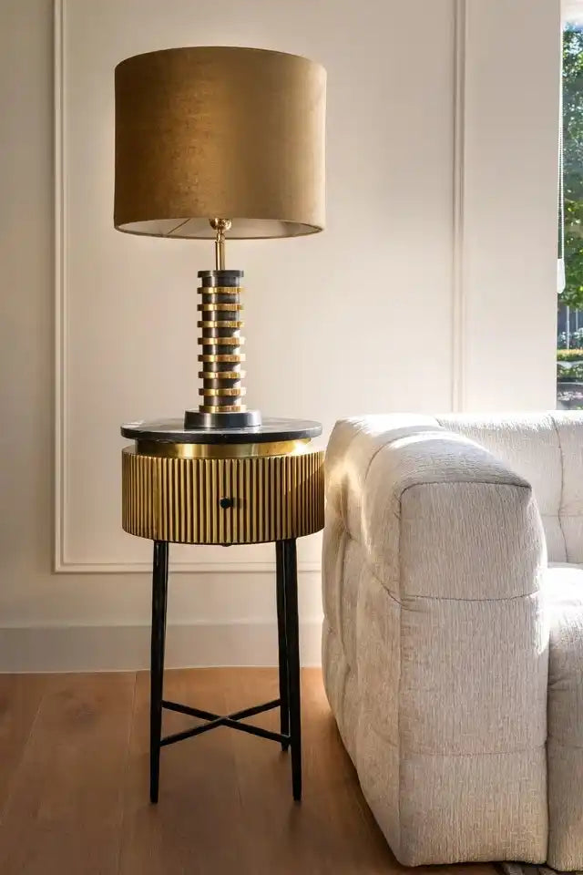 A modern brass and black bedside table lamp with a fluted cylindrical base and a cylindrical lampshade.