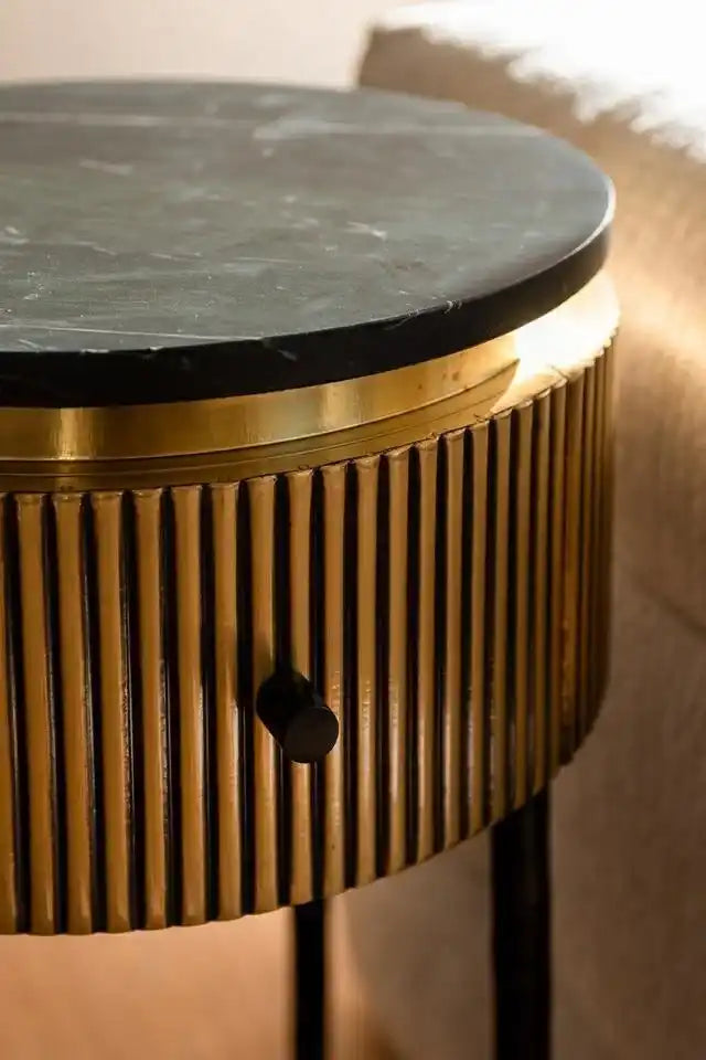 A round side table with a dark top, a ribbed brass body, and a small black knob.